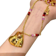 Collana lunga con pendente a cuore traforato color oro e texture particolare, con girocollo di perline di cristallo e pietra naturale.
