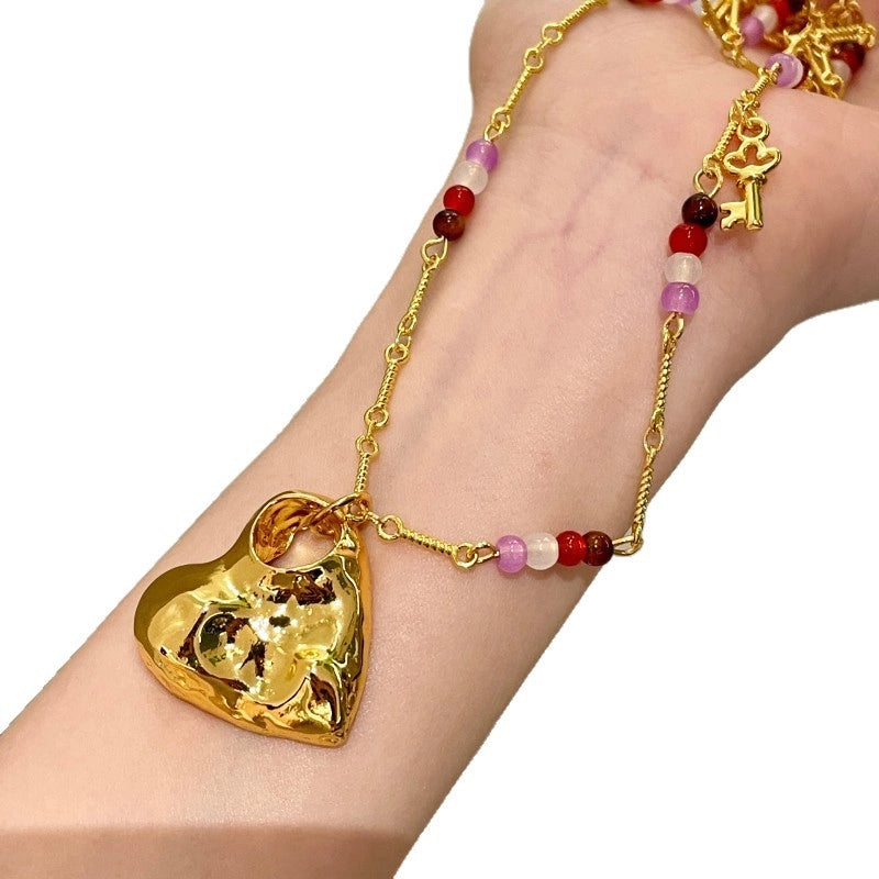 Collana lunga con pendente a cuore traforato color oro e texture particolare, con girocollo di perline di cristallo e pietra naturale.