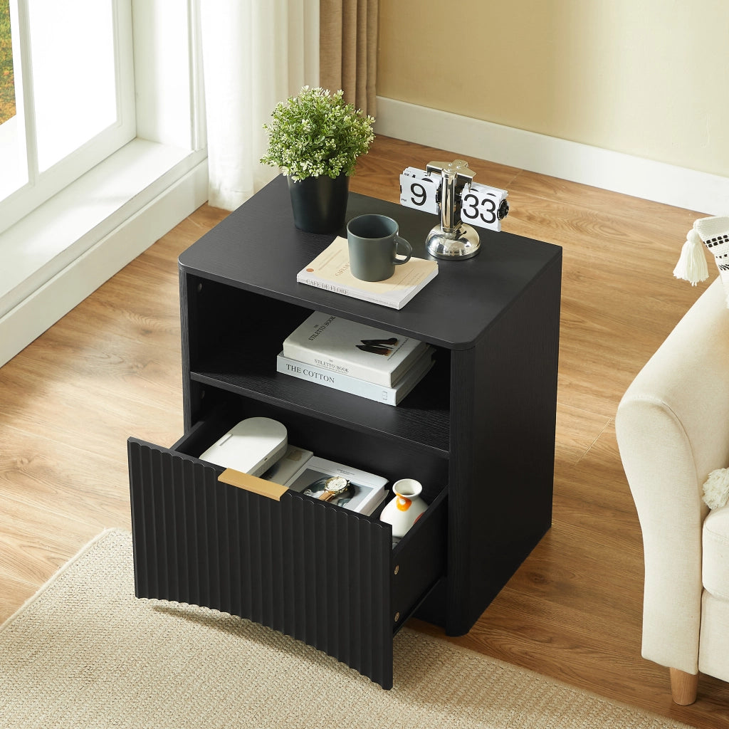 Comodino moderno in truciolare nero con cassetto aperto, maniglia dorata e design scanalato