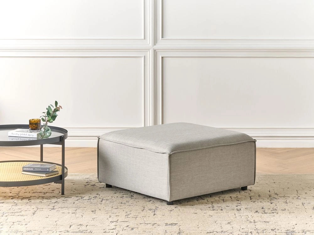 Ottomana imbottita in tessuto beige di forma quadrata con gambe nere stile moderno