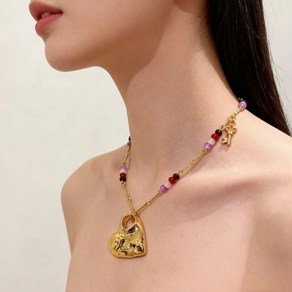 Collana lunga con pendente a cuore traforato color oro e texture particolare, con girocollo di perline di cristallo e pietra naturale.