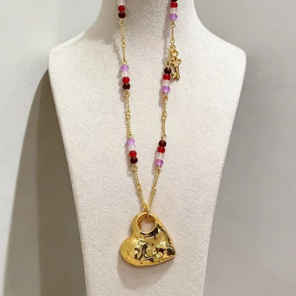 Collana lunga con pendente a cuore traforato color oro e texture particolare, con girocollo di perline di cristallo e pietra naturale.