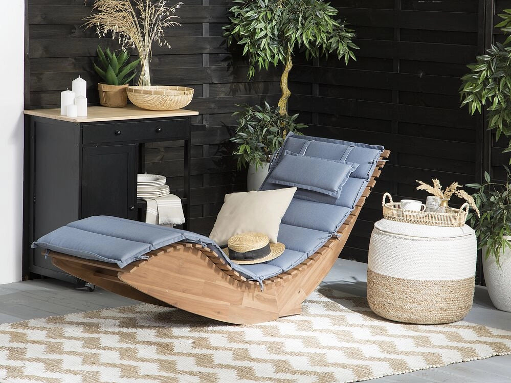Lettino prendisole a doghe in legno di acacia chiaro con design a dondolo a forma curva con cuscino di seduta blu