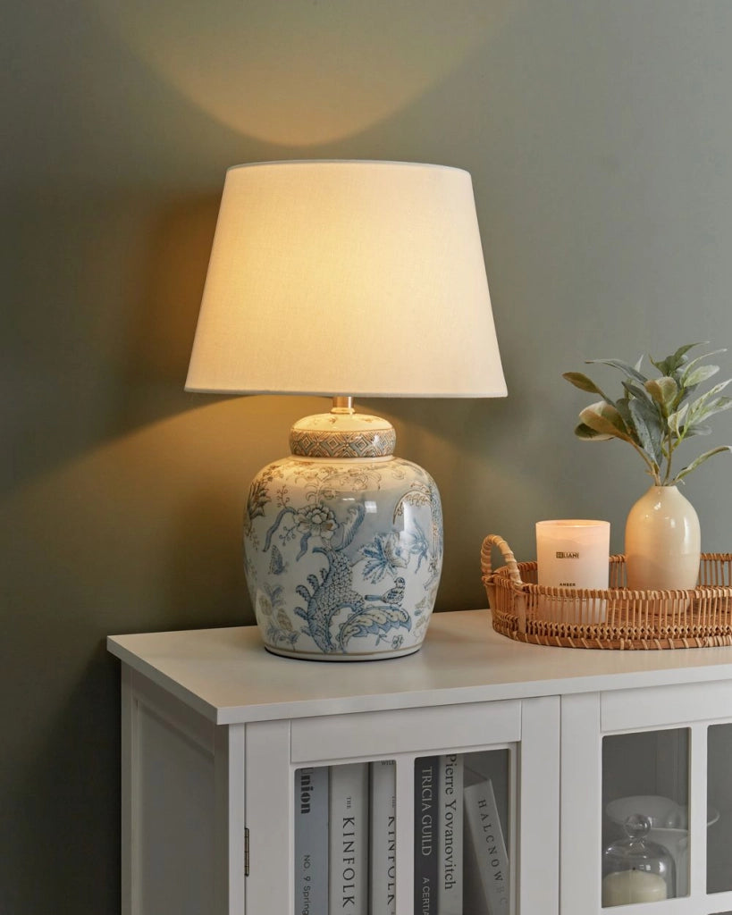 Lampada da tavolo con base in porcellana bianca e blu, paralume cilindrico in lino con un motivo