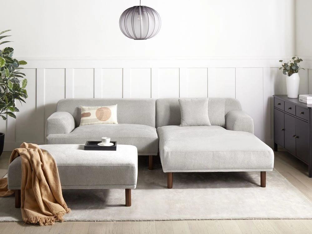 Divano ad angolo sinistro in tessuto grigio chiaro lato sinistro con pouf e gambe in legno stile minimalista